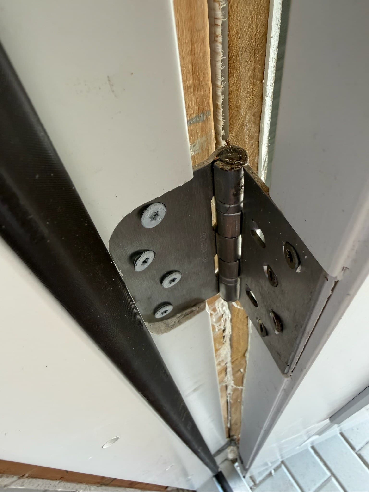 A close-up of a door hinge and jamb during a hardware repair, with visible screws and exposed wood