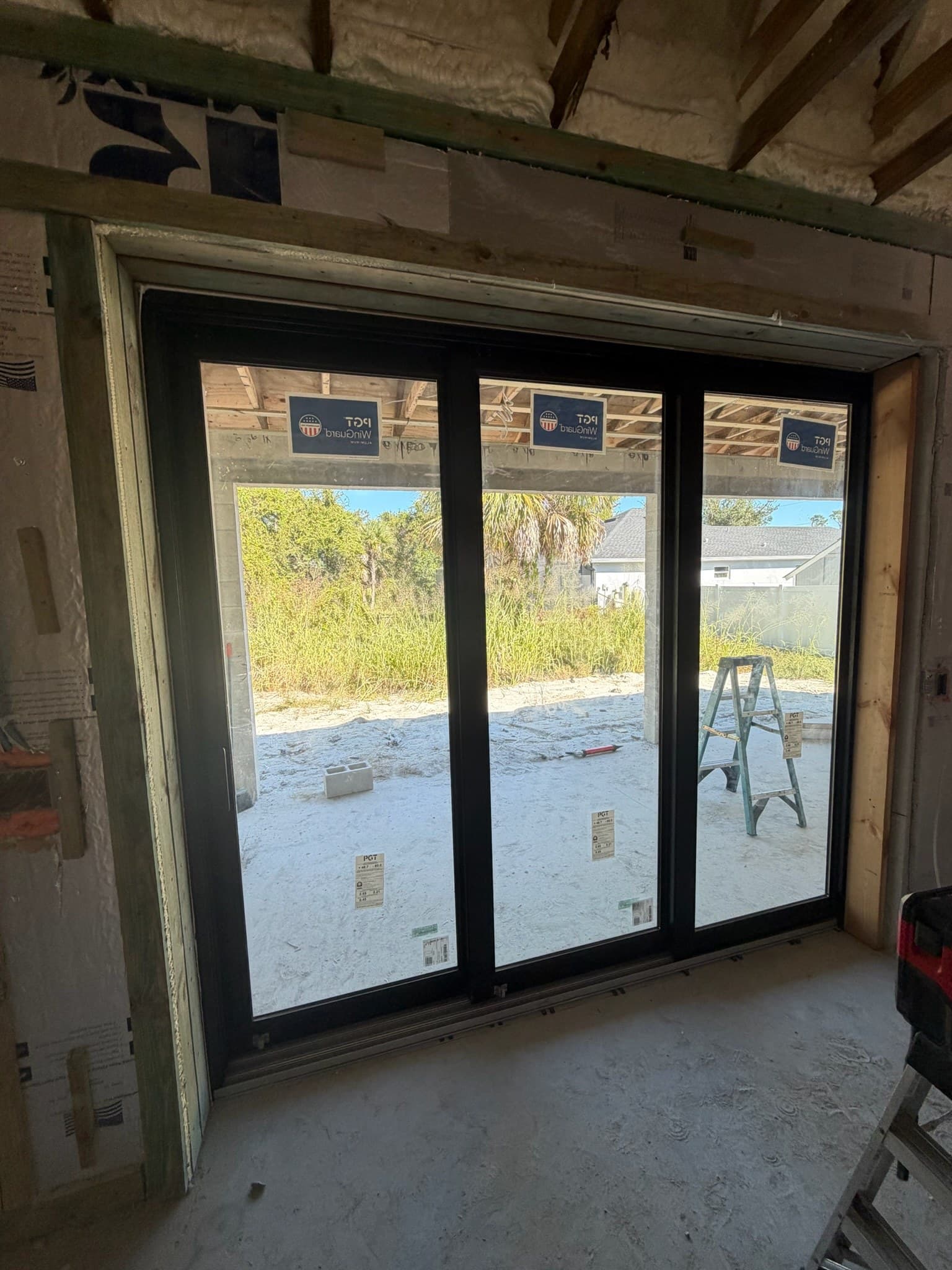A three-panel black-framed sliding glass door being installed in a house under construction