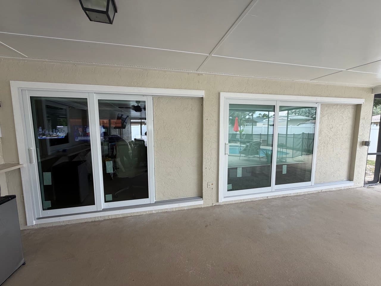 Two newly installed white sliding patio doors side by side under a covered patio, factory stickers still on the glass