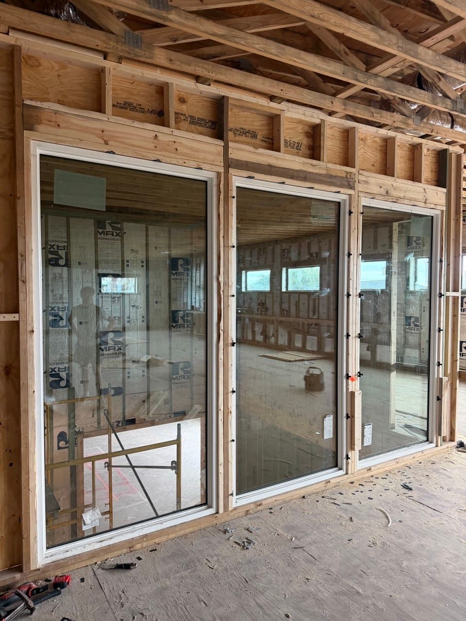 Large fixed windows and a slider set into a framed exterior wall during construction