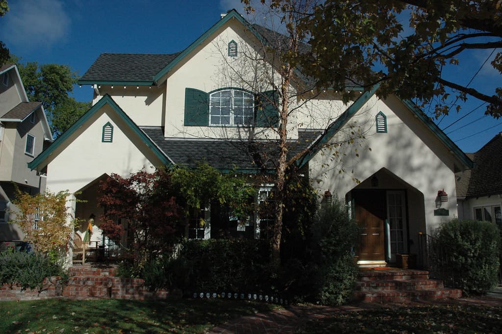 A stucco Tudor-style house with green shutters and steep gables